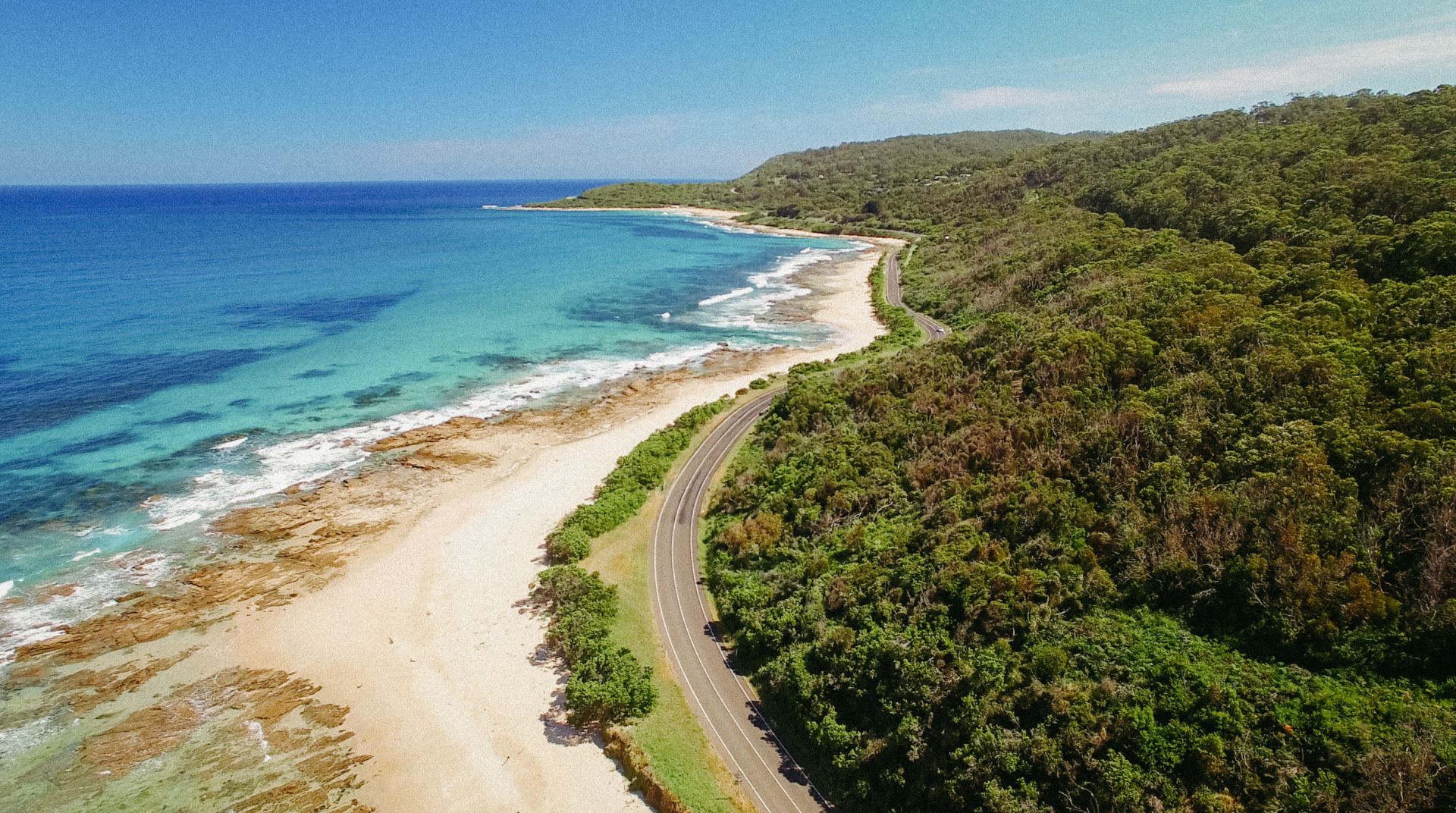 Image of a road alongside the ocean. It shows greenery on opposite side