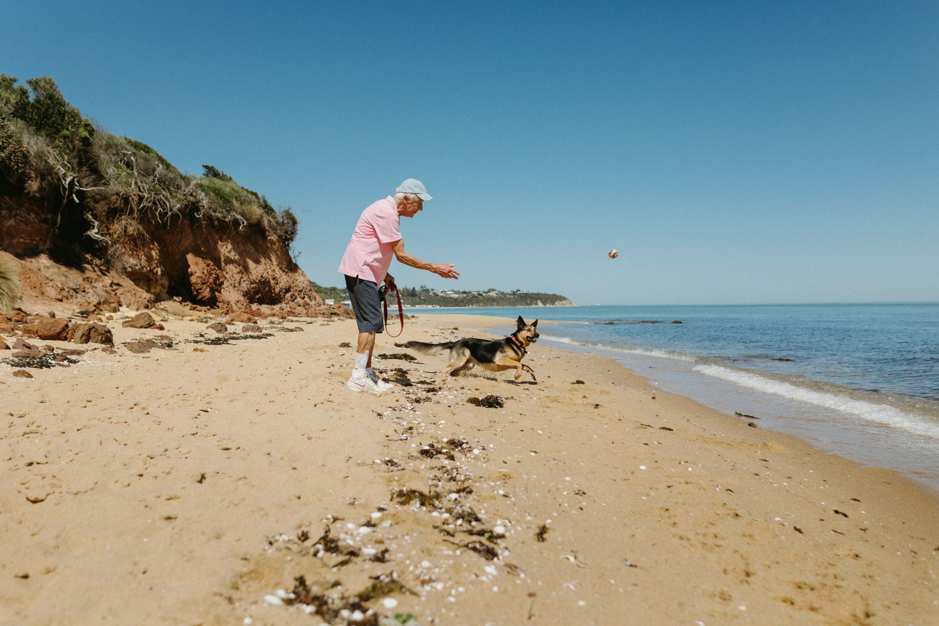 A woman in her 70's is seen throwing a ball to her dog on the beach