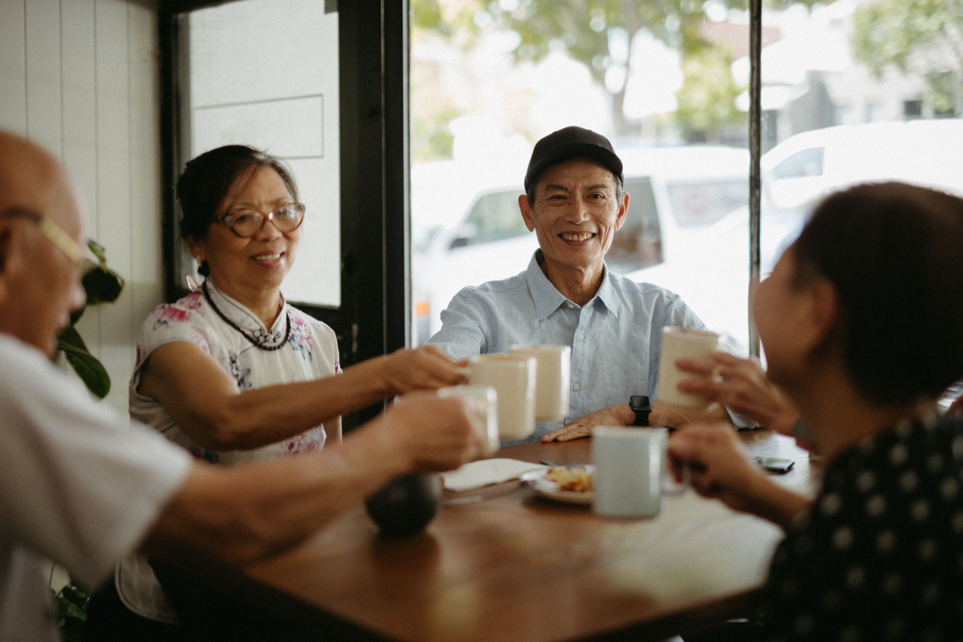 A man and Woman in their 50's are seen with raised coffee cups sitting at a cafe. 