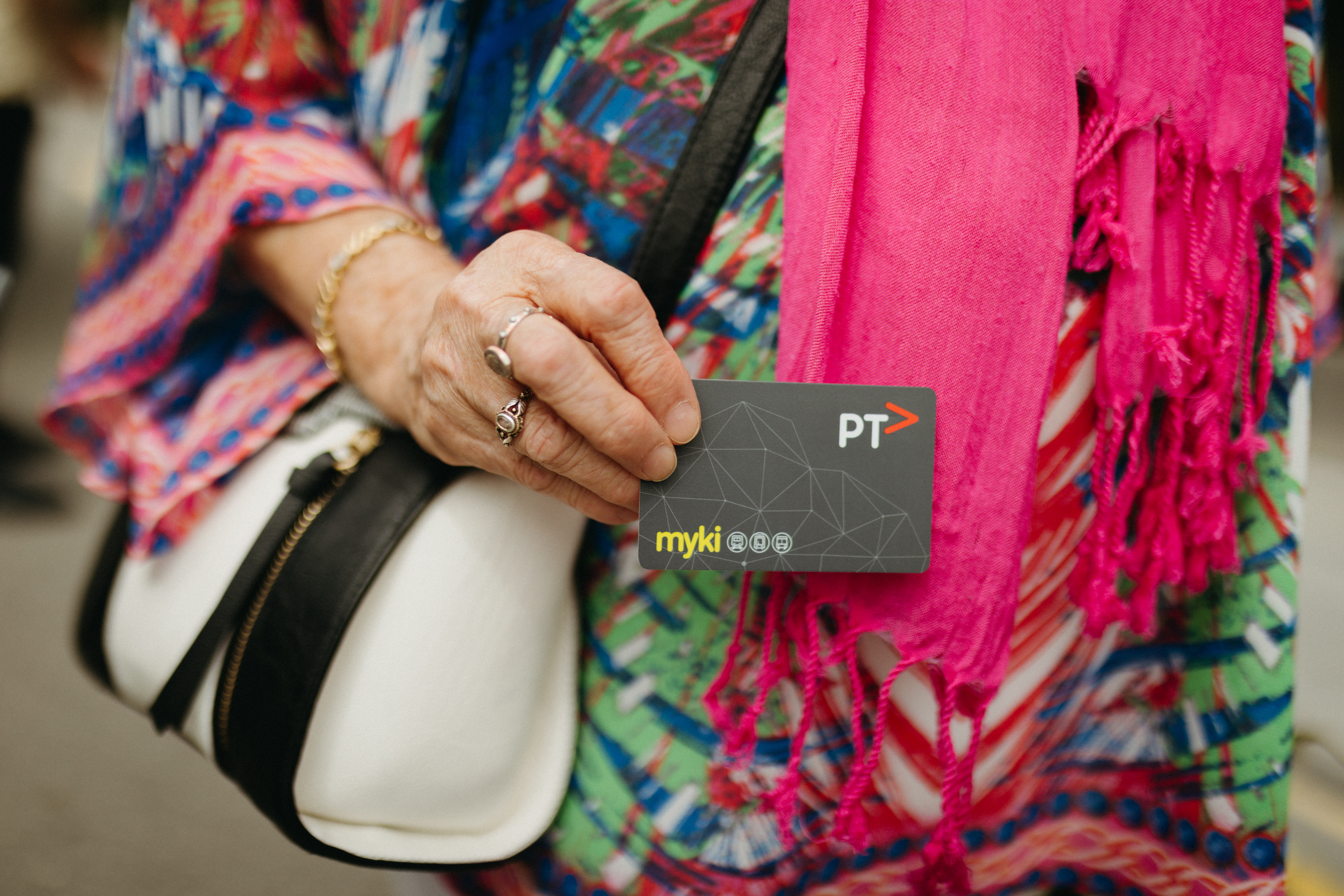 A close up of a womens hand who is wearing colourful clothing and holding a myki card. 