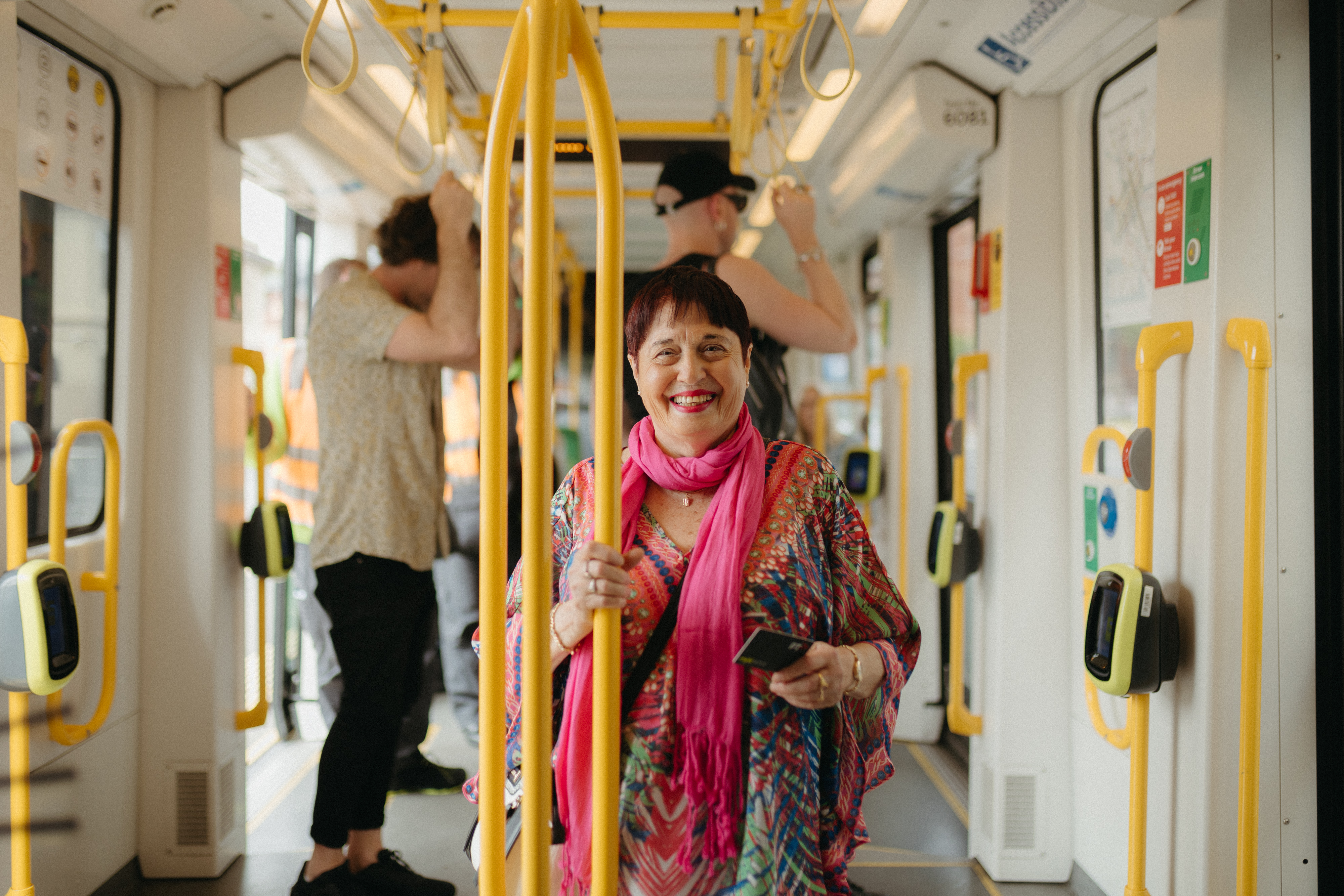Women in bright clothing smiling holding her myki card whilst travelling on the tram