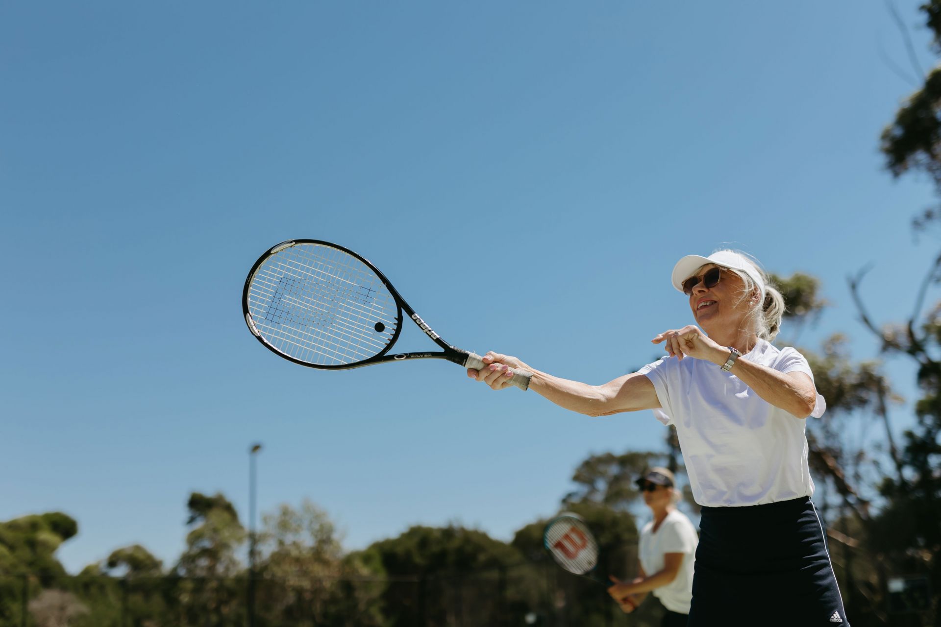 Lady in white clothing seen hitting a tennis ball with her raquet. 