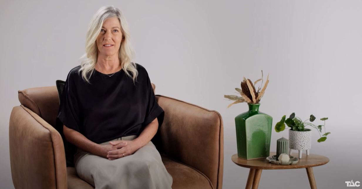 Image of a woman wearing a black top and a beige long skirt is sitting on a brown armchair